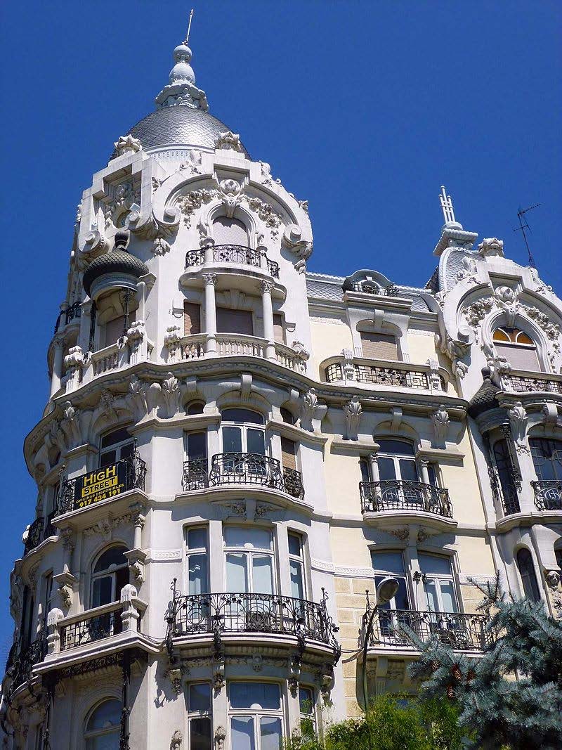 Fațada albă a clădirii Art Nouveau numită Casa Gallardo din Madrid, ilustrând balcoane curbate din fier forjat, ferestre ornamentate și o cupolă metalică pe colț.